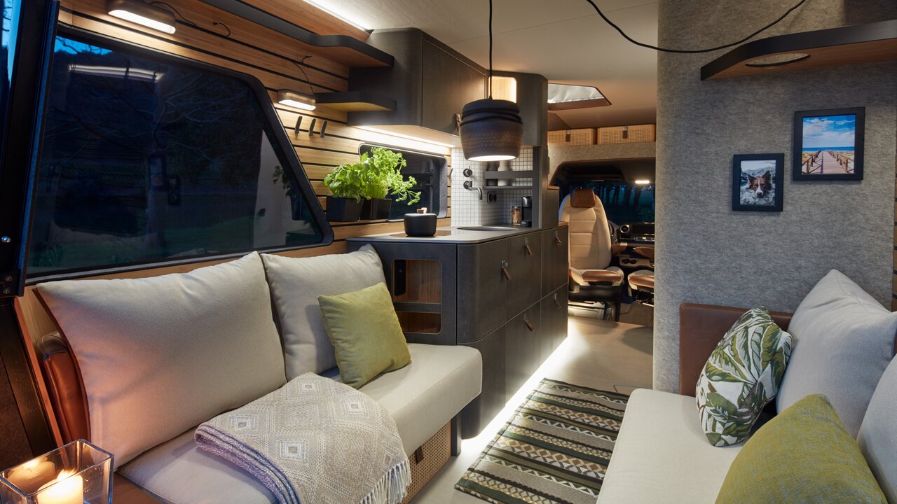Living area, kitchen and front of the VisionVenture, a concept vehicle from HYMER. The lights are on, it is dark outside the window. 