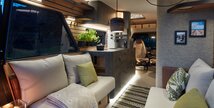 Living area, kitchen and front of the VisionVenture, a concept vehicle from HYMER. The lights are on, it is dark outside the window. 