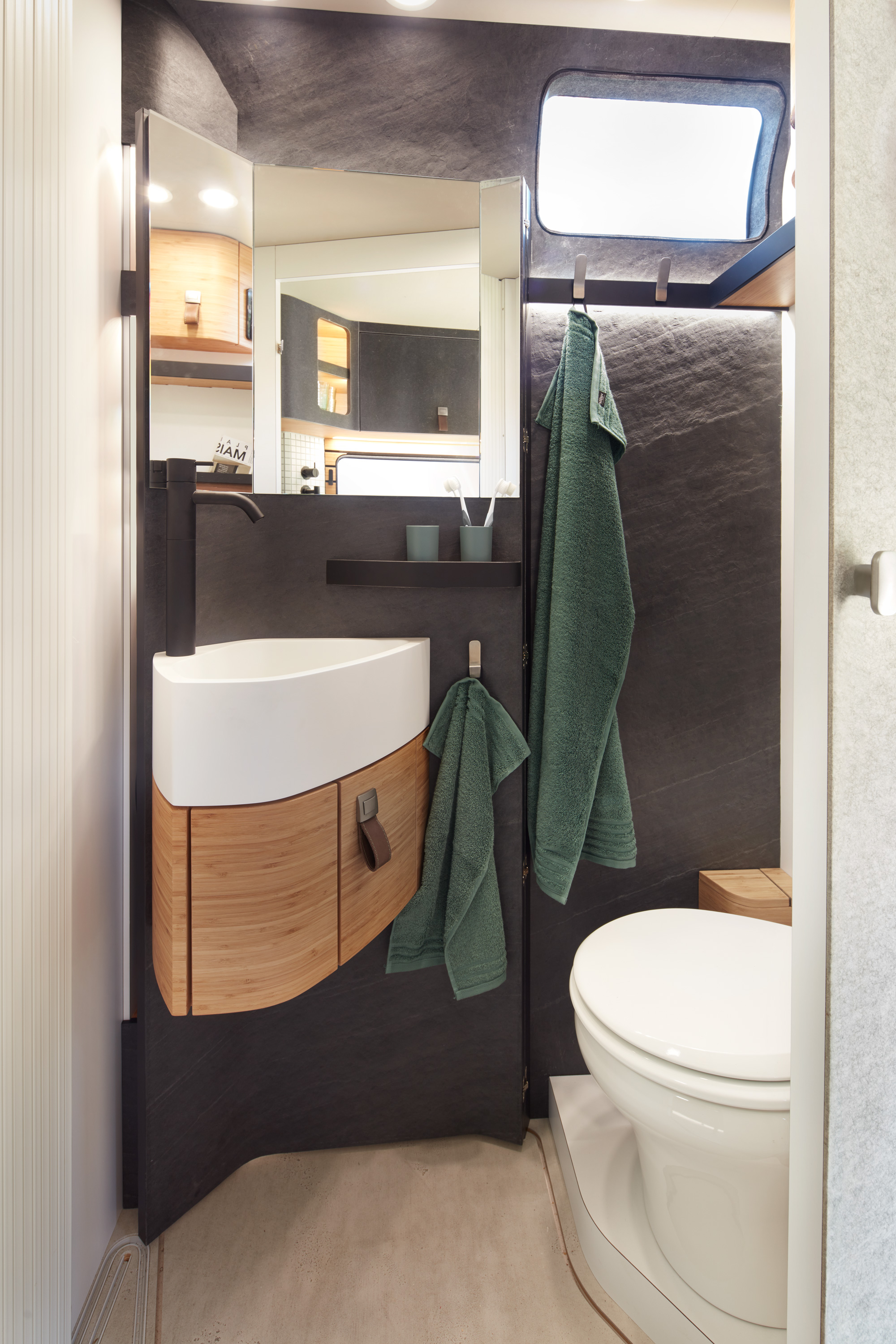 Weißes Waschbecken und Toilette im realisierten Konzeptfahrzeug von HYMER, VisionVenture. Die Wände sind in Schiefer, die Möbel in Holz gehalten.
